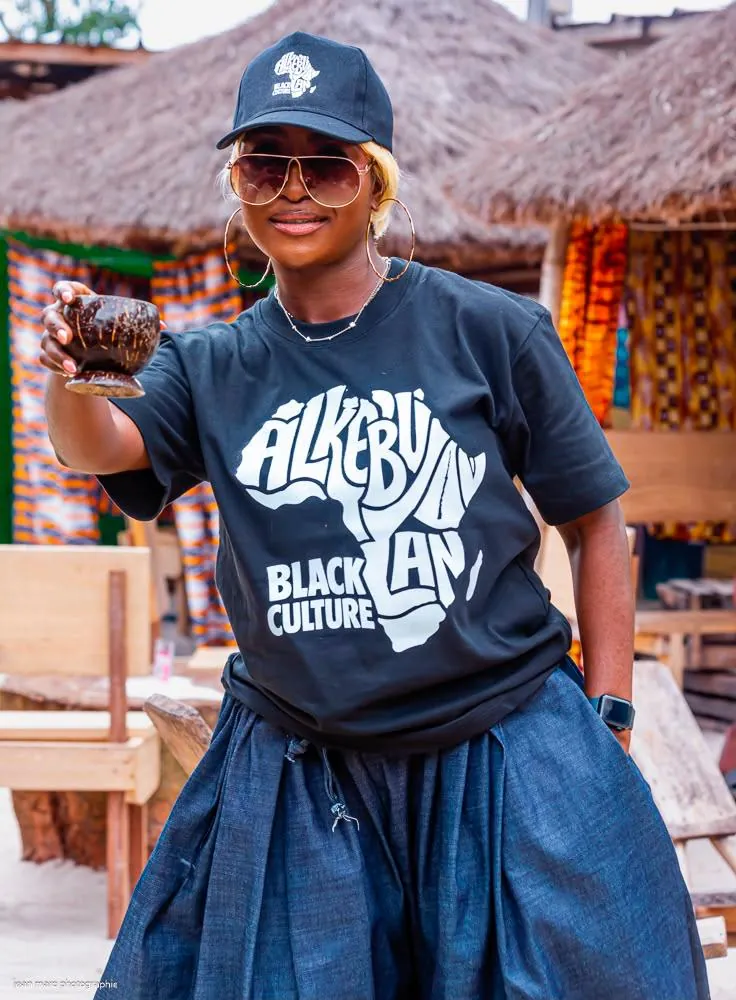 Femme en t-shirt Carte d'Afrique et casquette Alkebulan, tenant une calebasse